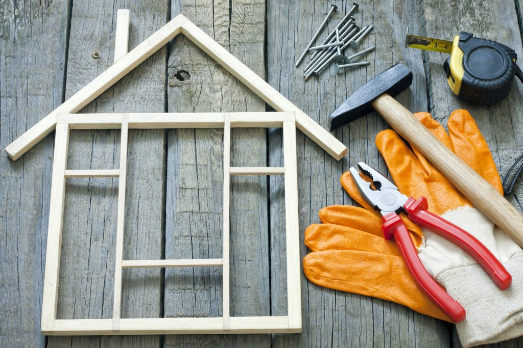 Maison en bois miniature posée sur un plancher avec des outils de bricolage à côté